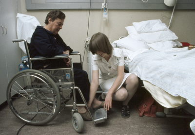828098 Afbeelding van een leerling-verpleegkundige die een patiënt in een rolstoel helpt op een van de ...